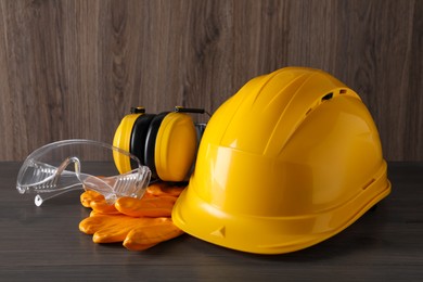 Photo of Hard hat, earmuffs, goggles and gloves on wooden table. Safety equipment