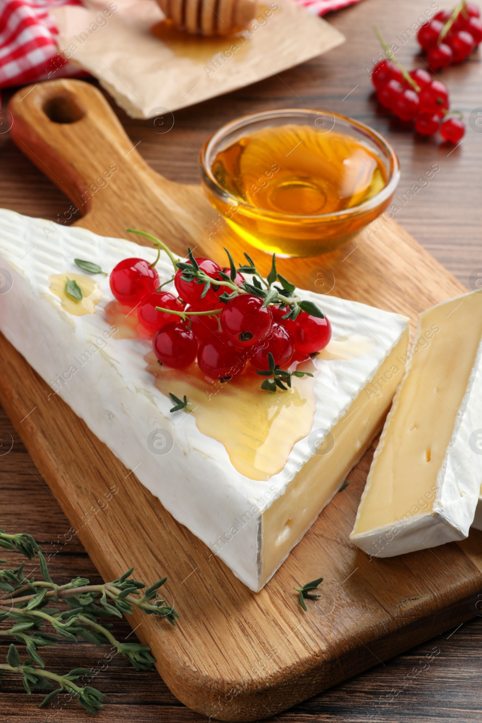 Photo of Brie cheese served with red currants and honey on wooden table, closeup