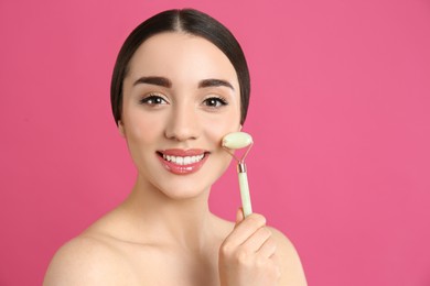 Photo of Woman using natural jade face roller on pink background, space for text