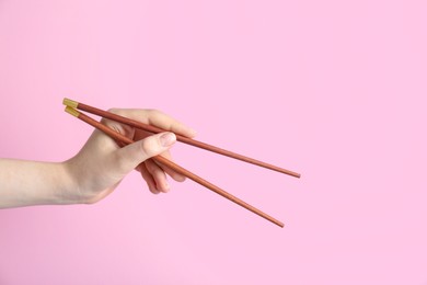 Woman holding pair of wooden chopsticks on pink background, closeup