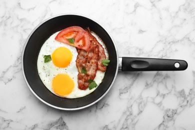 Photo of Fried sunny side up eggs with tomato and bacon in pan on marble background, top view