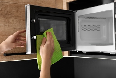 Photo of Woman cleaning microwave oven with rag in kitchen, closeup