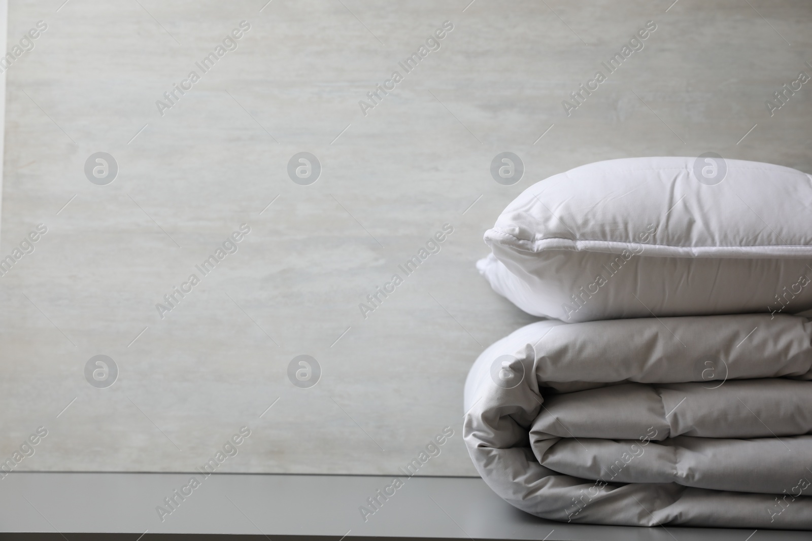 Photo of Soft folded blanket and pillow on light grey table, closeup. Space for text
