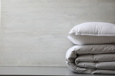 Photo of Soft folded blanket and pillow on light grey table, closeup. Space for text