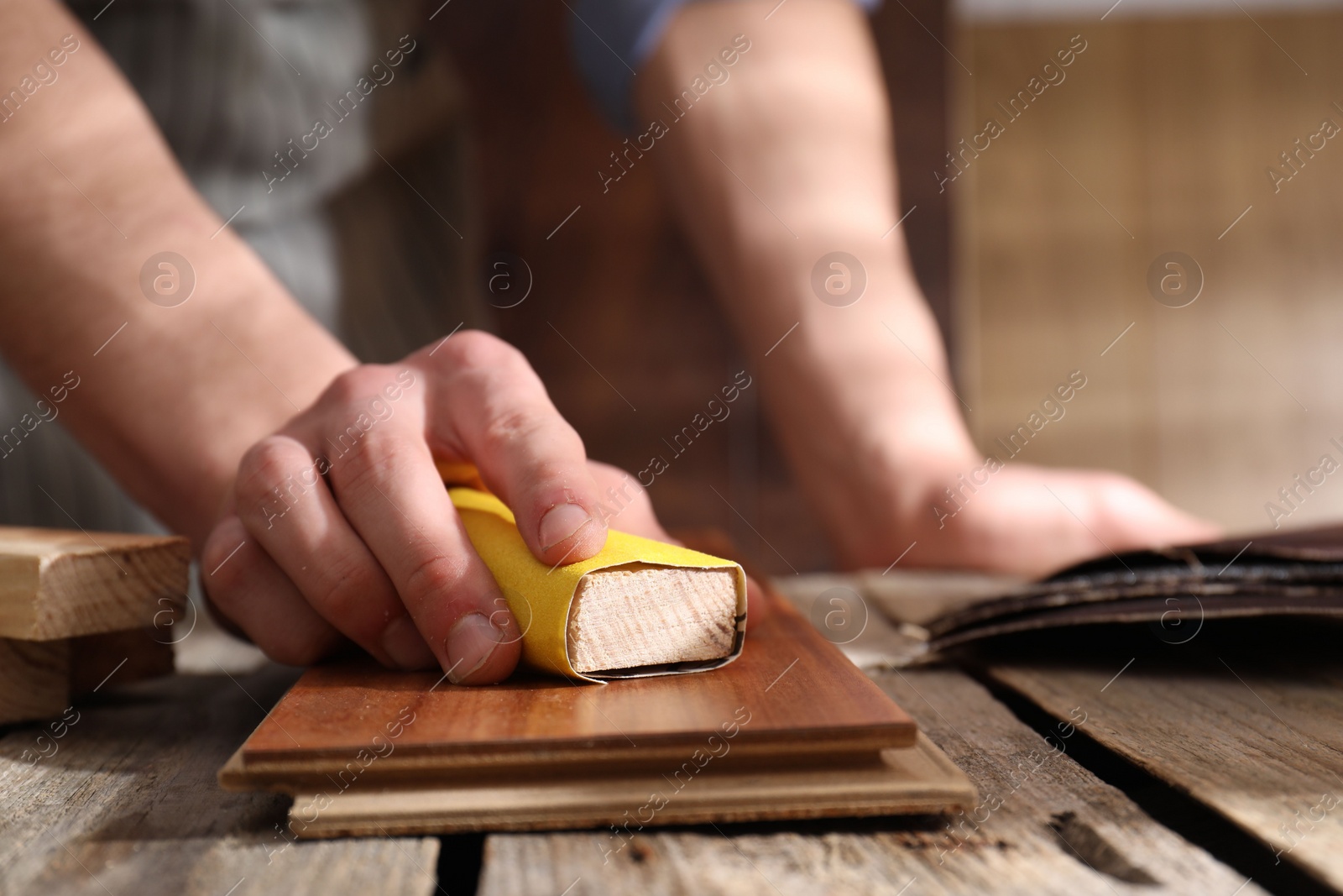 Photo of Man polishing wooden plank with sandpaper at table indoors, closeup