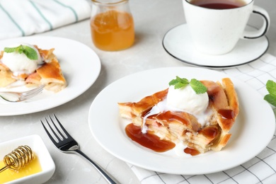 Slice of traditional apple pie with ice cream served on light marble table