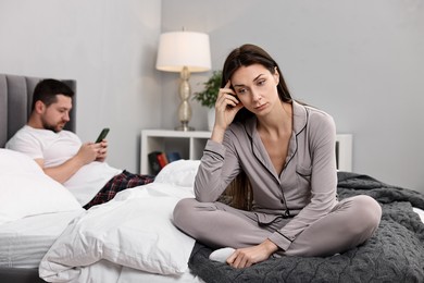 Stressed wife after quarrel with her husband sitting on bed, selective focus. Relationship problems