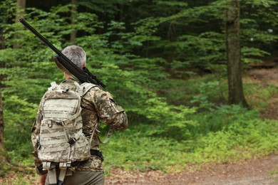 Photo of Man with hunting rifle wearing camouflage in forest, back view. Space for text