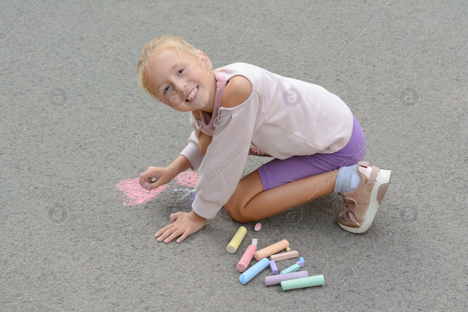 Photo of Little child drawing butterfly and heart with chalk on asphalt