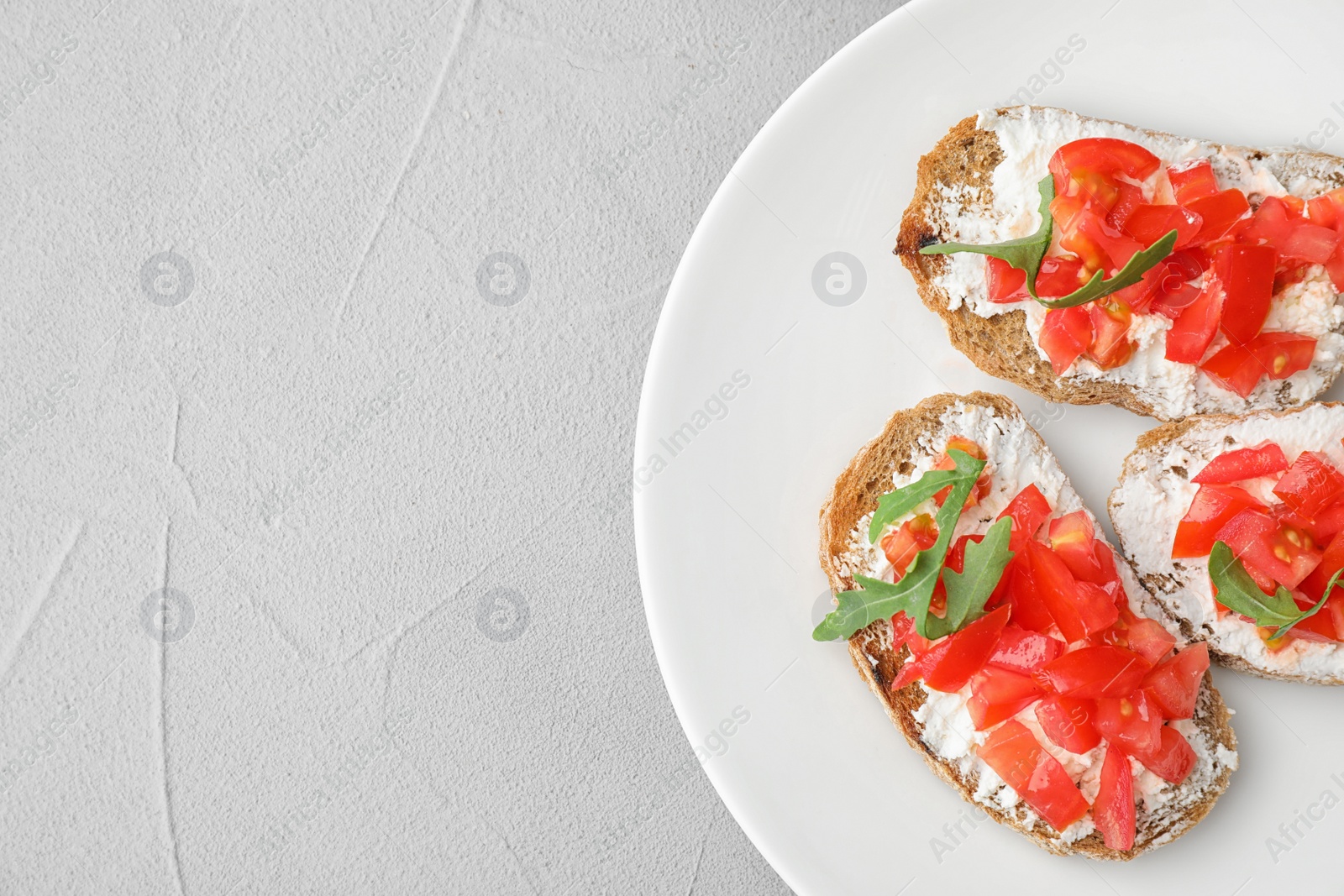 Photo of Plate of delicious tomato bruschettas on light grey background, top view. Space for text