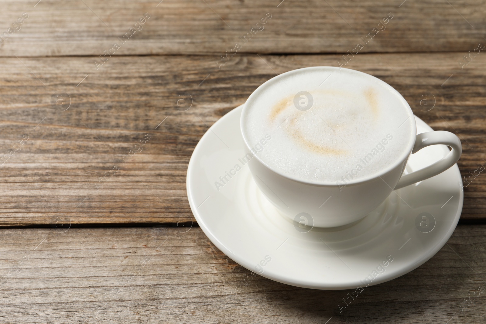Photo of Tasty cappuccino in coffee cup on wooden table, closeup. Space for text