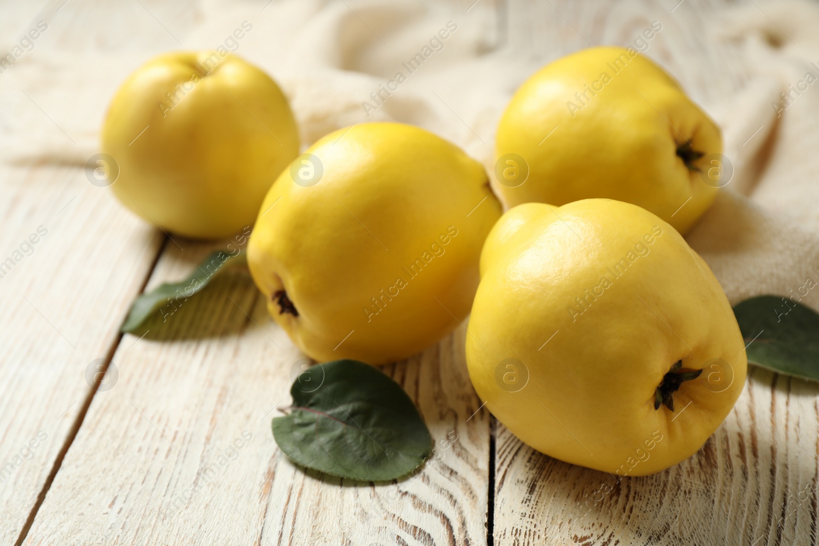 Photo of Fresh ripe organic quinces with leaves on white wooden table, closeup