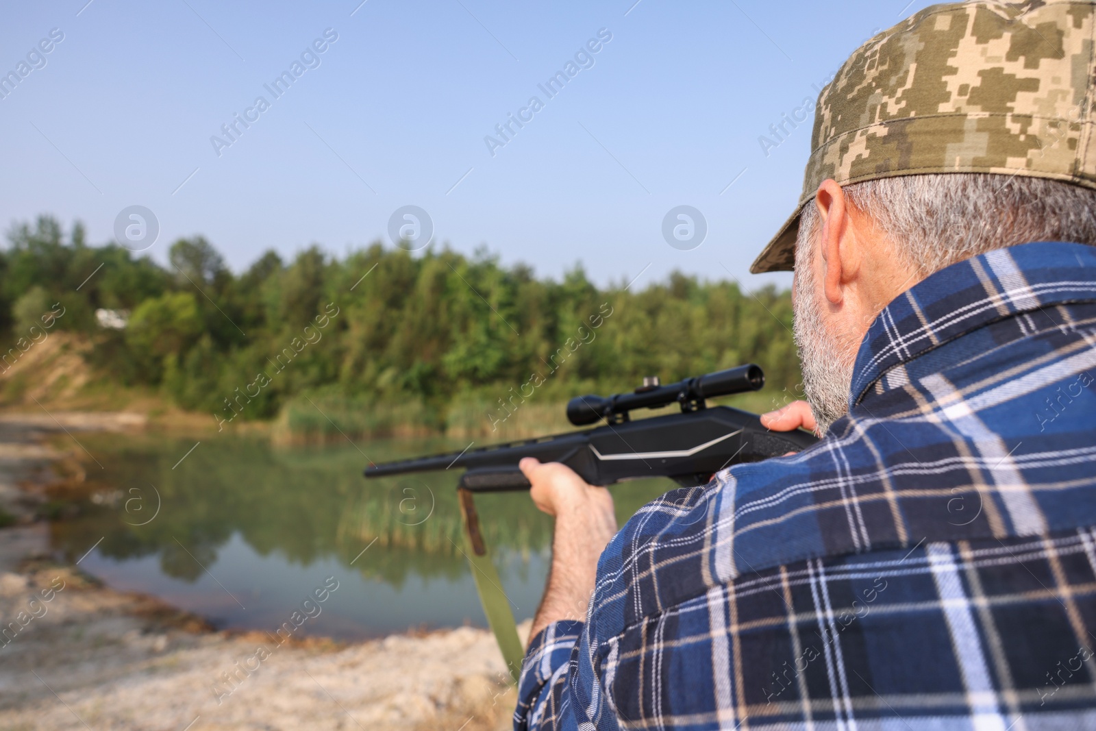 Photo of Man with hunting rifle near lake outdoors, back view. Space for text