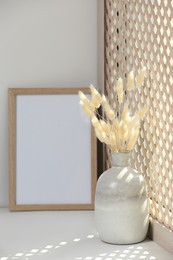 Photo of Blank photo frame and vase with dried plant on white window sill