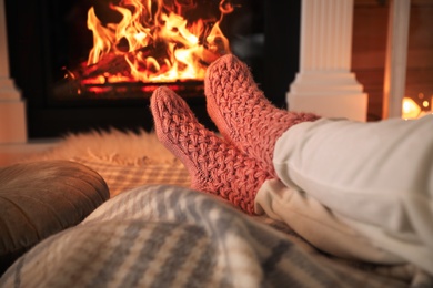 Photo of Woman in warm socks having rest near fireplace, closeup