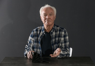 Photo of Poor elderly man with empty wallet and coins at table on dark background