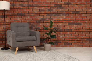 Photo of Cosy armchair, lamp and potted plant near brick wall in room, space for text. Interior design