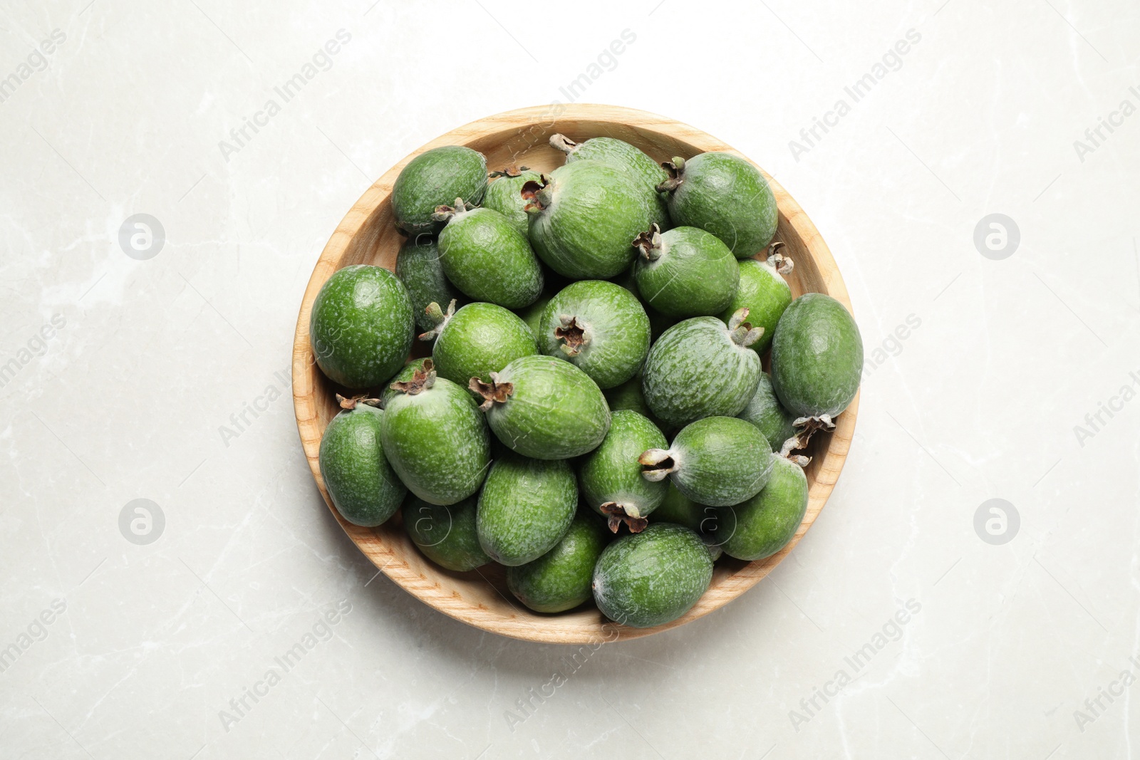 Photo of Fresh green feijoa fruits in bowl on light table, top view