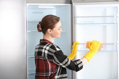 Photo of Woman in rubber gloves cleaning refrigerator at home