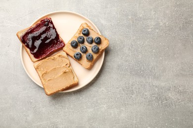 Photo of Tasty peanut butter sandwiches with jam and fresh blueberries on gray table, top view. Space for text