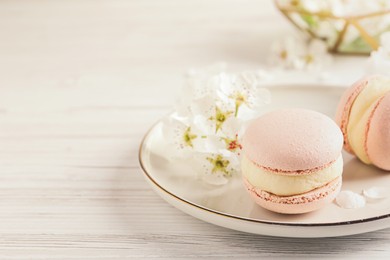 Photo of Delicious pink macarons and flowers on white wooden table, closeup. Space for text