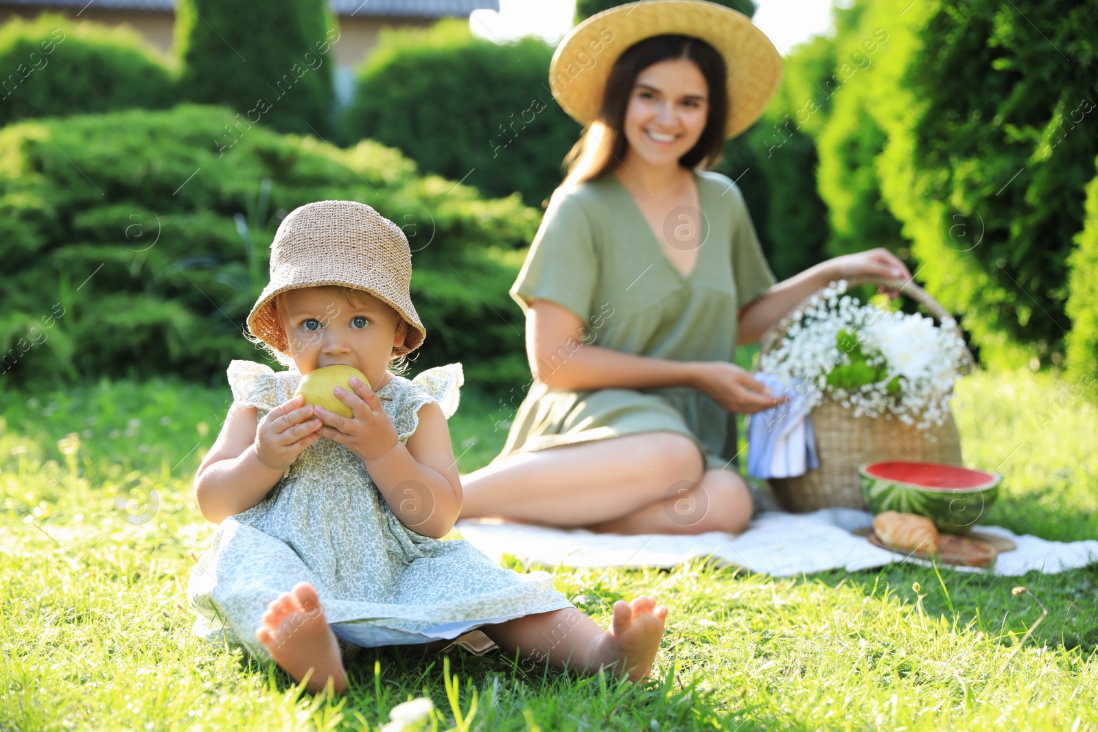 Photo of Mother and her daughter having picnic in garden, focus on baby with apple