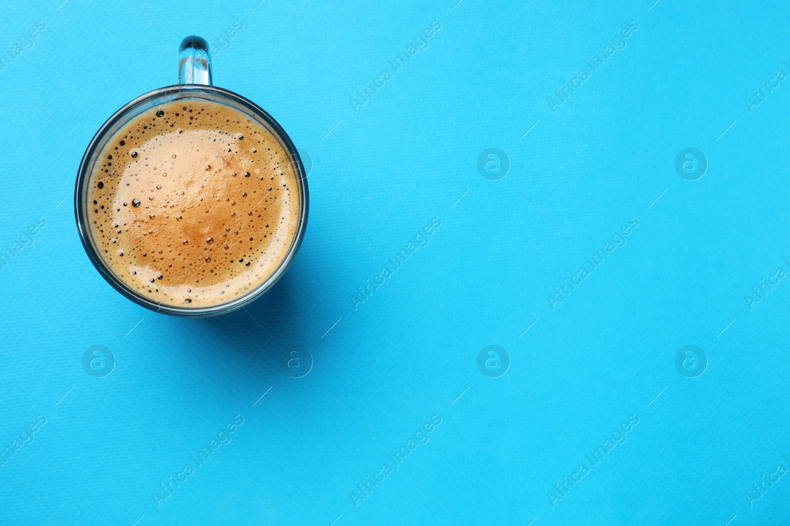 Photo of Fresh coffee in cup on light blue background, top view. Space for text