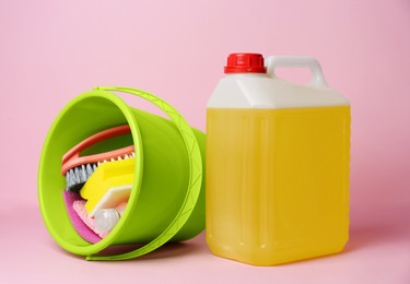 Photo of Green bucket with tools and canister of detergent on pink background. Cleaning supplies