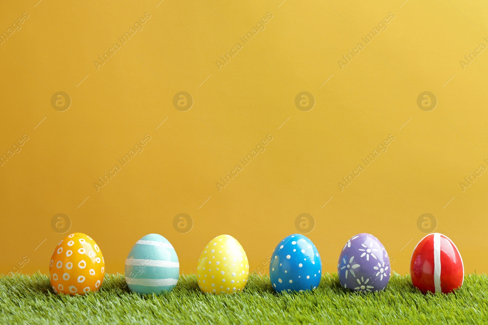 Photo of Painted Easter eggs on green grass against color background, space for text