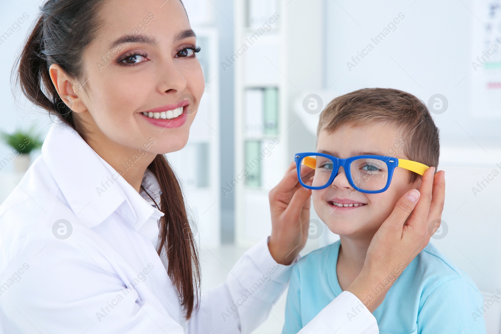 Photo of Children's doctor putting glasses on little boy in clinic