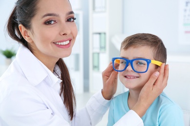 Children's doctor putting glasses on little boy in clinic