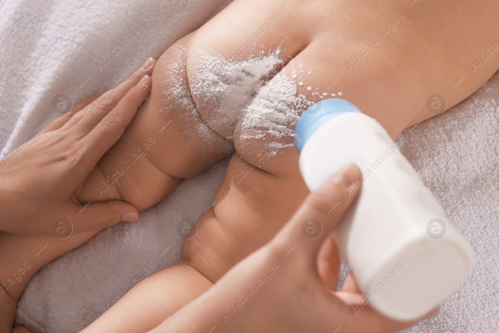 Photo of Mother applying dusting powder onto her baby on towel, above view