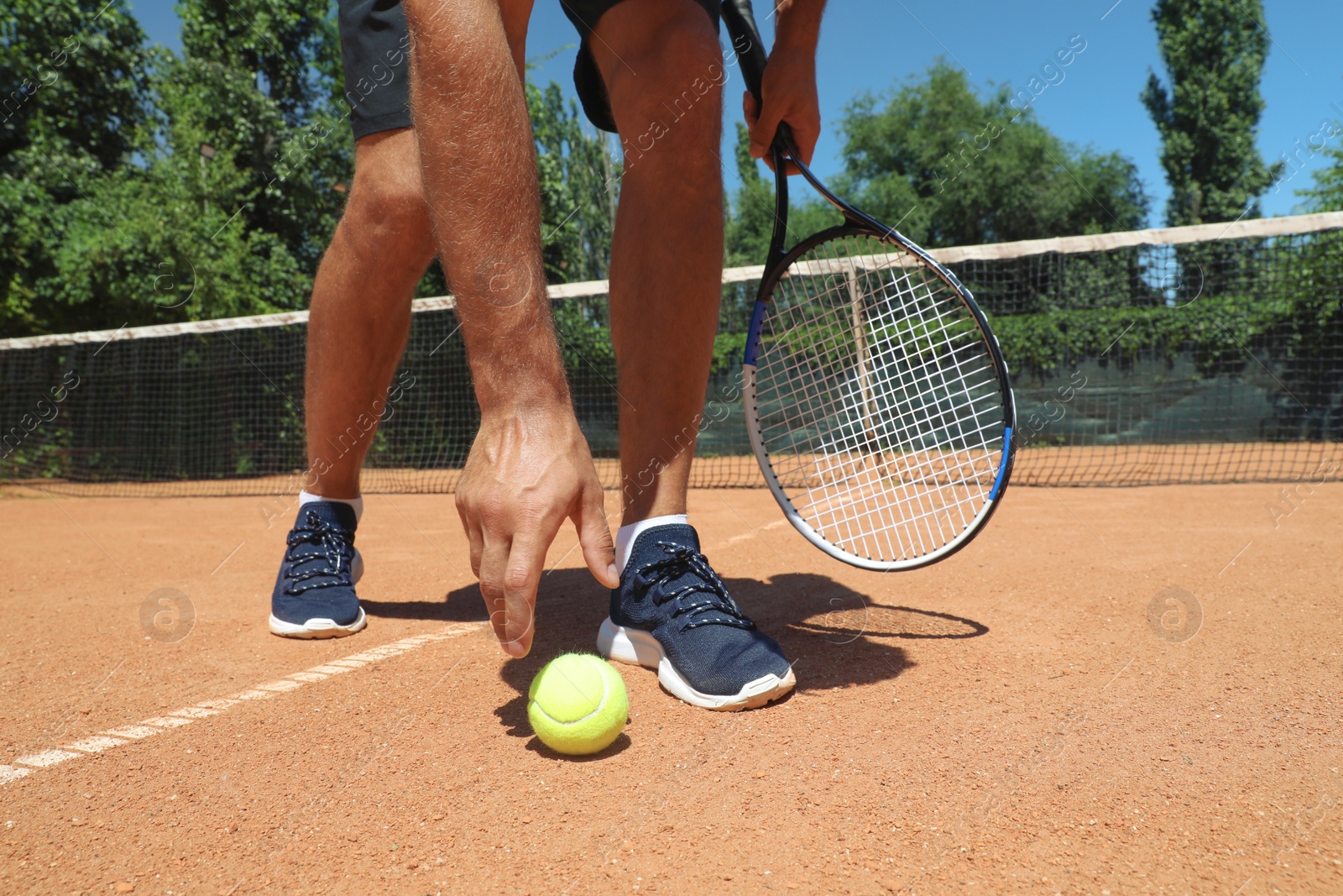 Photo of Man picking up tennis ball on court, closeup