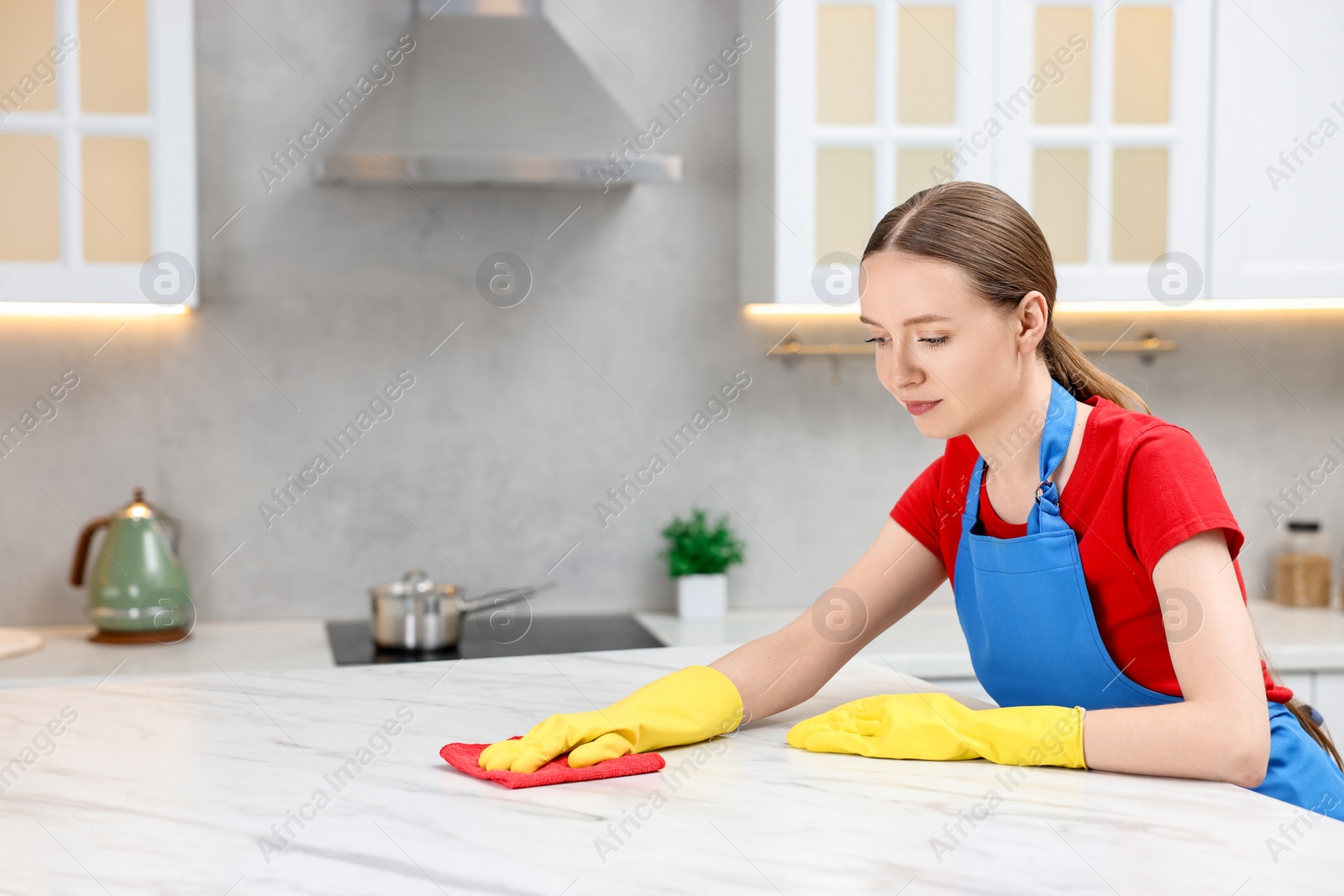 Photo of Woman cleaning white marble table with rag in kitchen, space for text