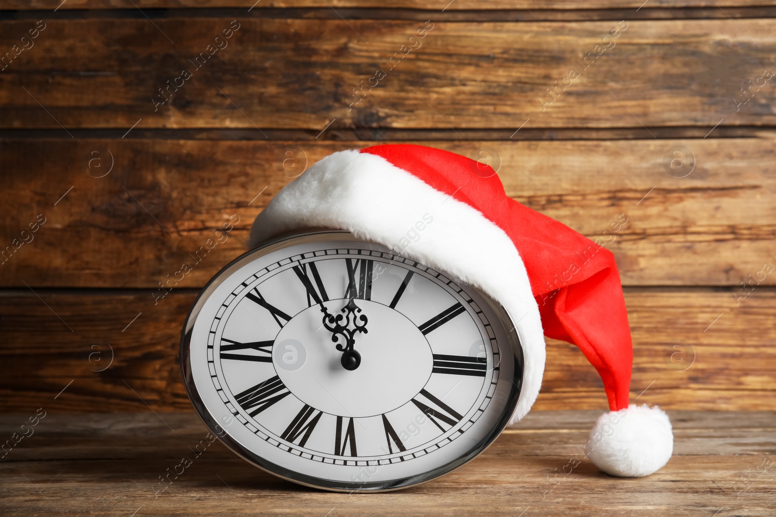 Photo of Clock with Santa hat showing five minutes until midnight on wooden background. New Year countdown