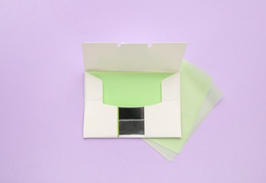 Package with facial oil blotting tissues on violet background, flat lay. Mattifying wipes