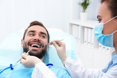 Photo of Dentist examining young man's teeth with mirror and probe in hospital
