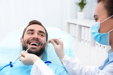 Dentist examining young man's teeth with mirror and probe in hospital