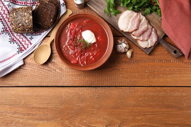 Photo of Clay bowl with Ukrainian borsch served on wooden table, flat lay. Space for text