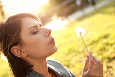 Young woman with dandelion in park on sunny day. Allergy free concept