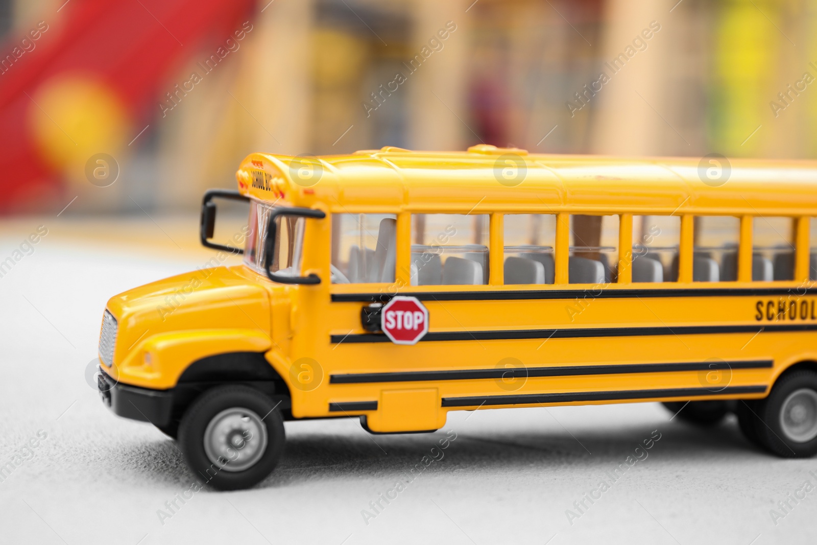 Photo of Yellow toy school bus against blurred 
background, closeup. Transport for students