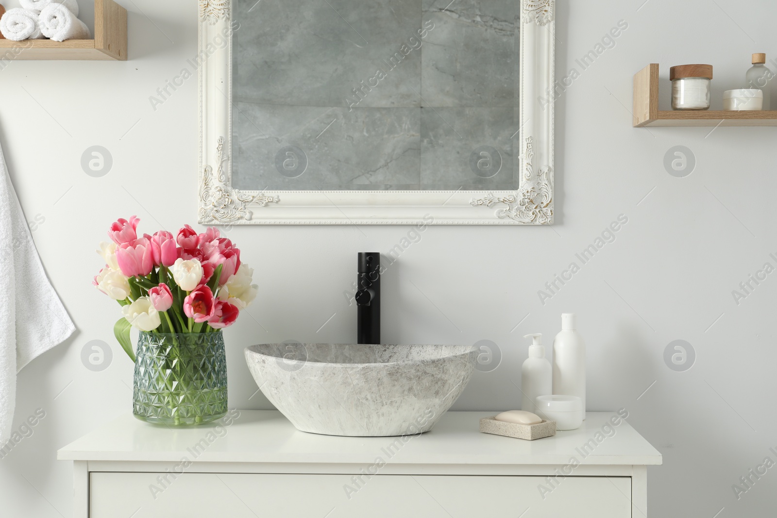 Photo of Vase with beautiful pink tulips and toiletries near sink in bathroom