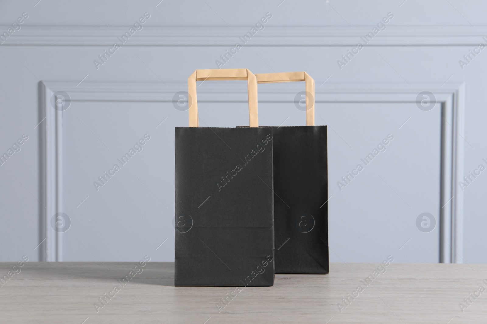 Photo of Black paper bags on wooden table against light grey wall