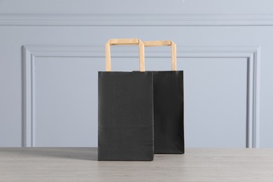 Photo of Black paper bags on wooden table against light grey wall