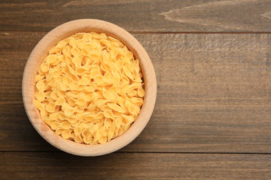 Photo of Raw farfalline pasta in bowl on wooden table, top view. Space for text