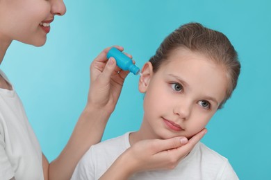 Mother dripping medication into daughter's ear on light blue background