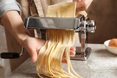 Photo of Young woman preparing noodles with pasta maker at table