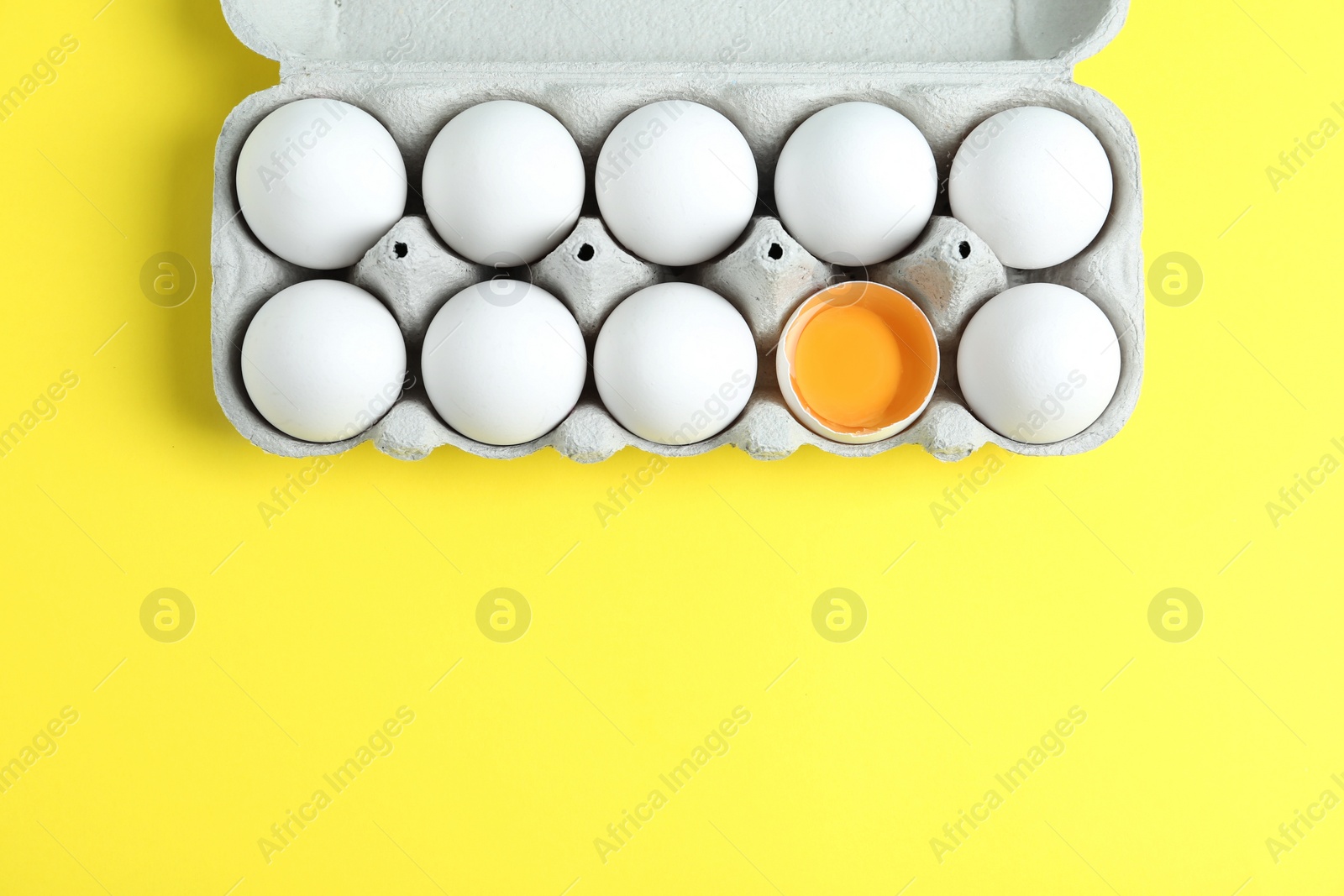 Photo of Fresh chicken eggs in box on yellow background, top view. Space for text