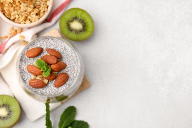 Delicious dessert with chia seeds, almonds and fresh cut kiwi fruits on light table, flat lay. Space for text