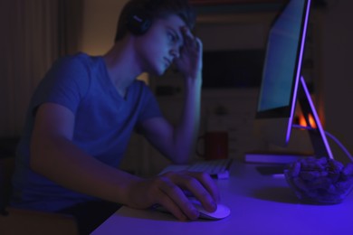 Photo of Teenage boy using computer in room at night, focus on hand. Internet addiction